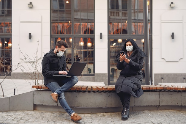 Menschen, die eine Schutzmaske tragen, die in einer Stadt mit elektronischen Geräten sitzt