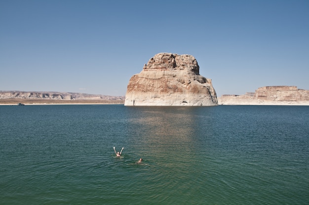 Menschen, die im Wasser nahe einem großen Felsen mit klarem Himmel schwimmen