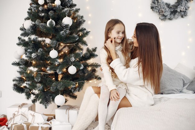 Menschen, die sich für Weihnachten reparieren. Mutter spielt mit ihrer Tochter. Familie sitzt auf einem Bett. Kleines Mädchen in einem weißen Kleid.