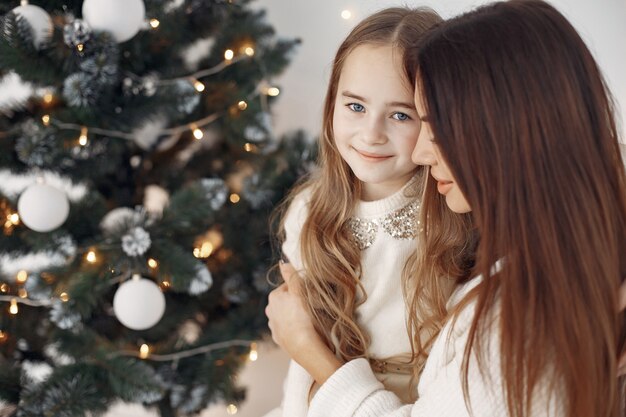 Menschen, die sich für Weihnachten reparieren. Mutter spielt mit ihrer Tochter. Familie sitzt auf einem Bett. Kleines Mädchen in einem weißen Kleid.