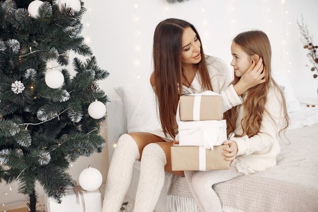 Menschen, die sich für Weihnachten reparieren. Mutter spielt mit ihrer Tochter. Familie sitzt auf einem Bett. Kleines Mädchen in einem weißen Kleid.