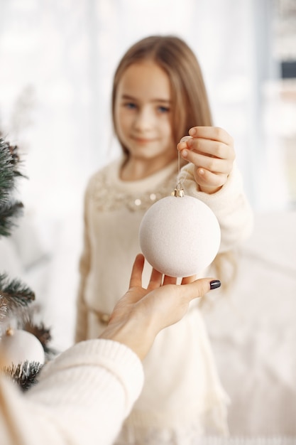 Menschen, die sich für Weihnachten reparieren. Mutter spielt mit ihrer Tochter. Familie verzierter Weihnachtsbaum. Kleines Mädchen in einem weißen Kleid.