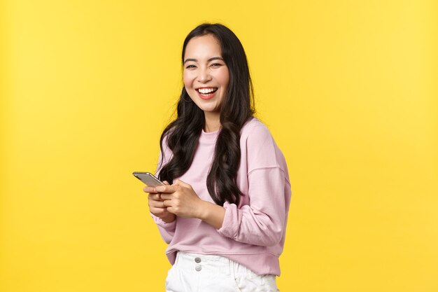 Menschen Emotionen, Lifestyle-Freizeit- und Schönheitskonzept. Fröhlich lächelnde glückliche asiatische Frau, drehen Sie sich in die Kamera und lachen Sie, nachdem Sie einen lustigen Beitrag in der Social-Media-App gelesen haben und ein Smartphone halten.