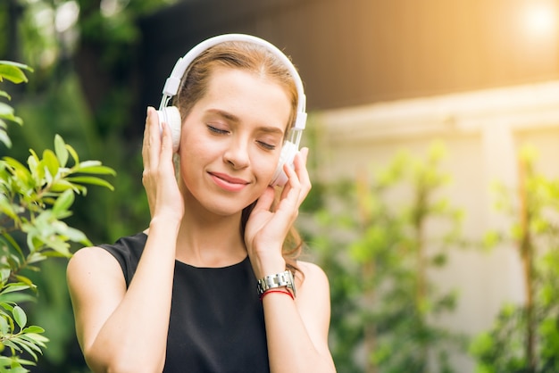 Menschen Freizeit-und Technologie-Konzept - Attraktive junge Frau Musik hören auf dem Musik-Player im Freien. Hipster Mädchen genießen die Melodien in ihren Kopfhörern in den Morgen Park. Objektiv Flare.