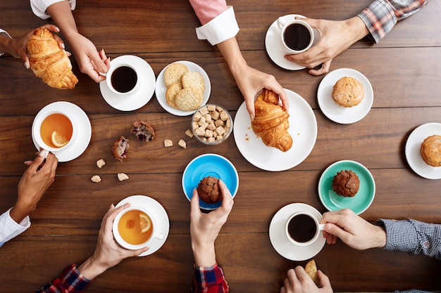 Menschen Hände auf Holztisch mit Croissants und Kaffee.