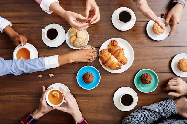 Menschen Hände auf Holztisch mit Croissants und Kaffee.