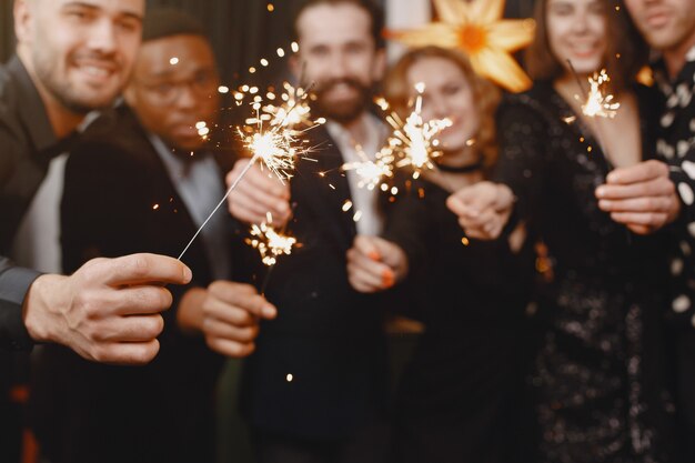 Menschen in einer Christman-Dekoration. Mann im schwarzen Anzug. Gruppenfeiern Neujahr. Menschen mit bengalischen Lichtern.