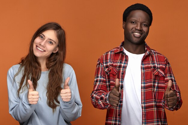 Menschen, Liebe, Freude, Glück und interracial Beziehungen Konzept. Zwei beste Freunde verschiedener Ethnien machen Daumen hoch Zeichen und lächeln, glücklich, sich nach langer Trennung zu sehen