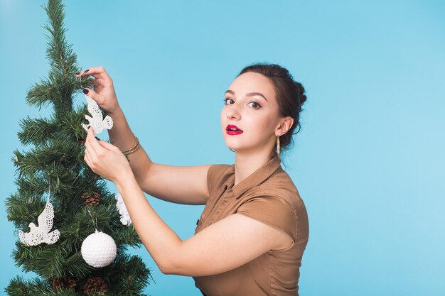 Menschen- und feiertagskonzeptporträt der lächelnden jungen frau mit weihnachtsbaum auf blauem hintergrund
