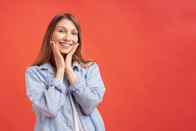 Menschengefühle - Porträt des überraschten positiven Mädchens über der roten Wand