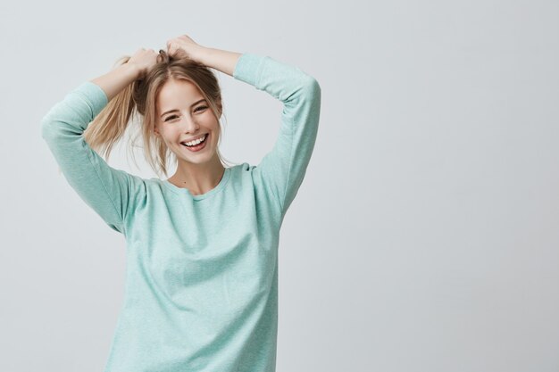 Menschliche Gesichtsausdrücke und Emotionen. Positive junge schöne Frau mit gefärbten blonden glatten Haaren im Pferdeschwanz gekleidet in Freizeitkleidung