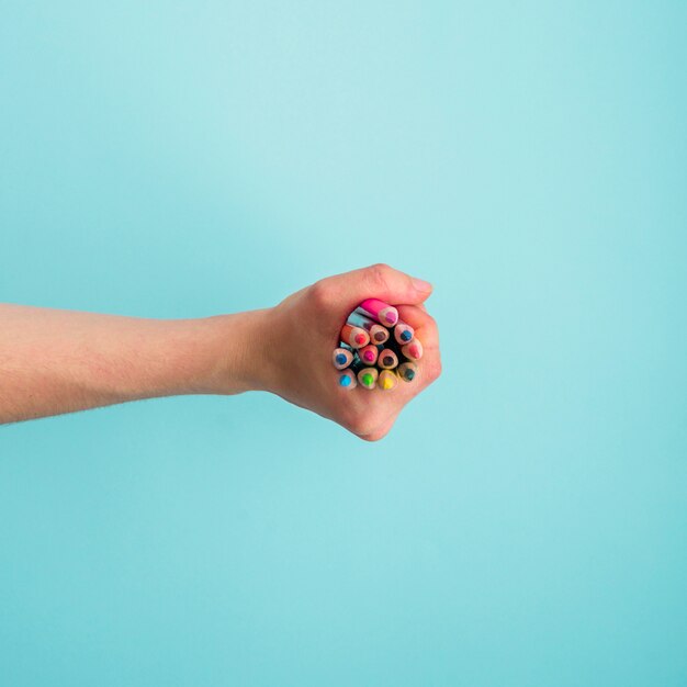 Menschliche Hand, die Bündel bunte Bleistifte auf blauem Hintergrund hält