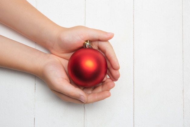 Menschliche Hand, die eine Weihnachtskugel auf hölzernem Weiß hält