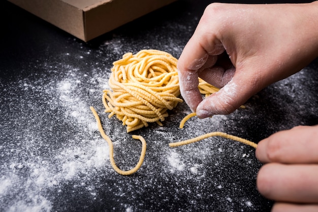 Menschliche Hand, die frische Spaghettiteigwaren mit Pulvermehl auf Küchenarbeitsplatte zubereitet