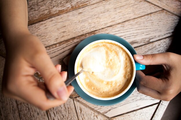 Menschliche Hand, die Kaffeelöffel hält und heißen Kaffee auf Holztisch rührt