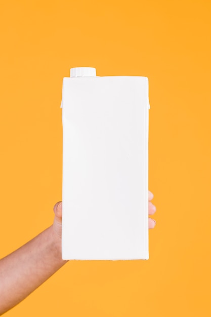 Menschliche Hand, die weißen Milchkasten auf gelbem Hintergrund anhält