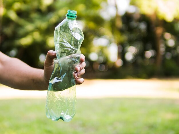 Menschliche Hand, die zerquetschte Plastikflasche an draußen hält