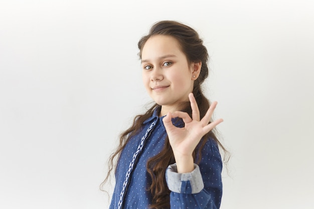 Menschliche Mimik und Körpersprachenkonzept. Bild des positiven glücklichen Teenager-Mädchens mit langen dunklen Haaren