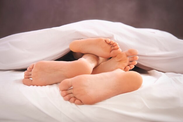 Menschliche nackte Füße und weiße Bettdecke