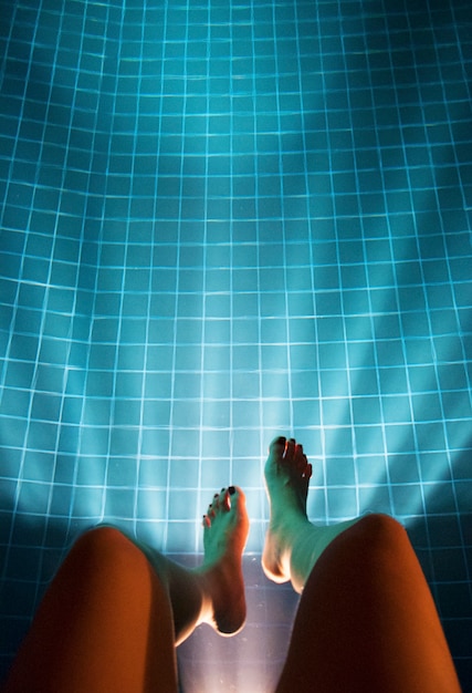 Kostenloses Foto menschliches bein, das hinunter swimmingpool-luftaufnahme hängt