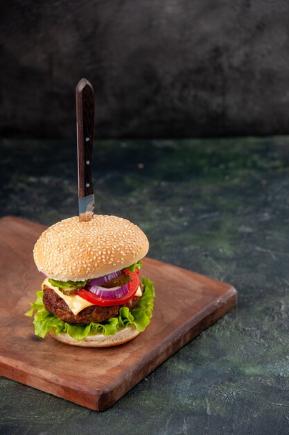 Messer in leckerem Fleischsandwich auf Holzbrett auf isolierter dunkler Oberfläche mit freiem Platz