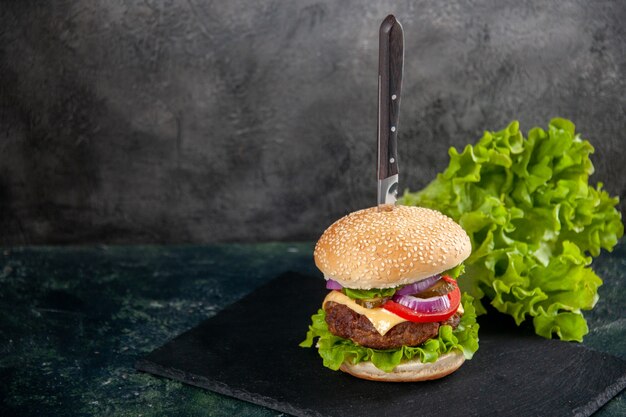 Messer in leckerem Fleischsandwich und grün auf schwarzem Tablett auf der linken Seite auf unscharfer Oberfläche mit freiem Platz