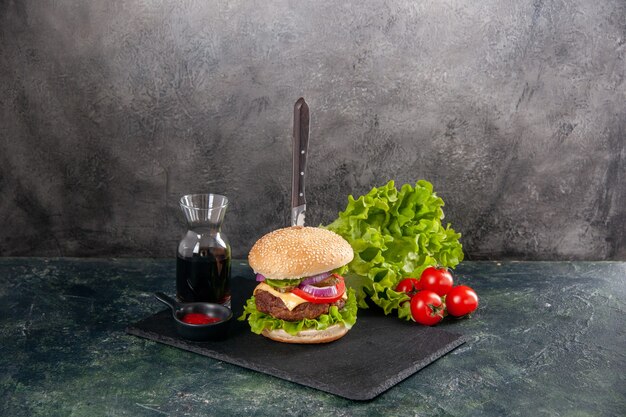 Messer in leckerem Fleischsandwich und grünem Pfeffer auf schwarzer Tablettsauce Ketchup-Tomaten mit Stiel auf grauer Oberfläche