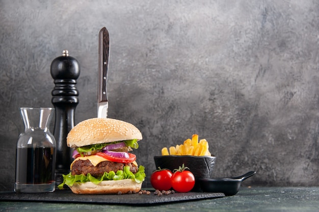 Messer in leckerem Fleischsandwich und grünem Pfeffer auf schwarzer Tablettsauce Ketchup-Tomaten mit Stielpommes auf der rechten Seite auf dunkler Oberfläche