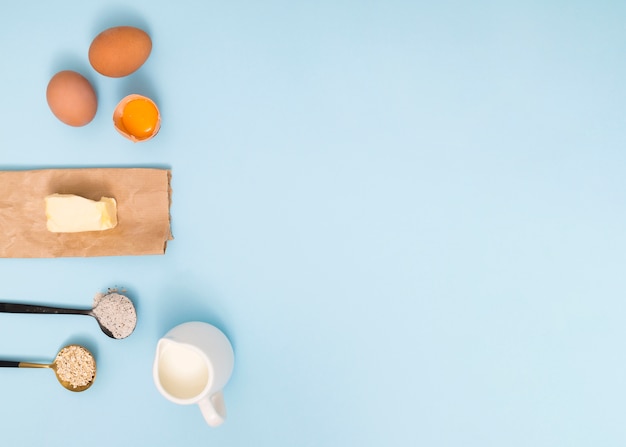 Messlöffel mit Haferstall; Mehl; Eier; Butter und Milch auf blauem Hintergrund