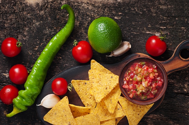 Mexikanische Nacho-Chips und Salsa tauchen in eine Schüssel auf Holz