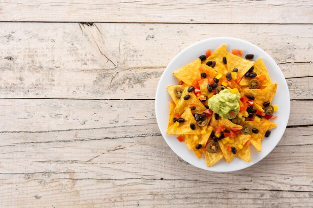 Mexikanische Nachos-Tortilla-Chips mit schwarzen Bohnen, Guacamole, Tomate und Jalapeno auf Holztisch