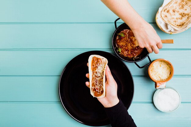 Mexikanisches Nahrungsmittelkonzept mit den Händen, die Burrito vorbereiten