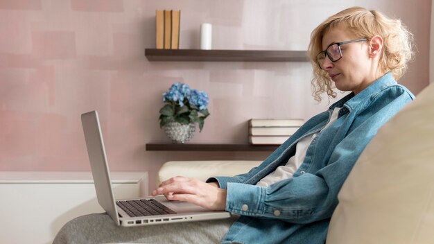 Mid Shot Frau sitzt auf der Couch und arbeitet am Laptop