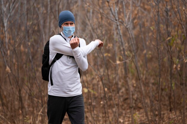 Mid Shot Mann mit Gesichtsmaske im Wald streckt die Arme
