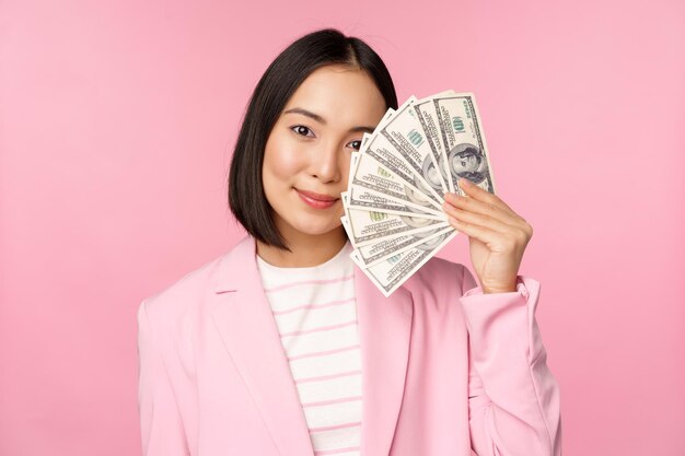 Mikrokreditinvestitionen und Geschäftsleute Konzept Junge asiatische Geschäftsfrau Corporate Lady zeigt Geld Bargeld Dollar lächelnd erfreut rosa Hintergrund