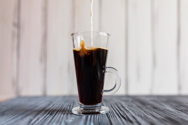 Milch gießt in Kaffee in Latte Glas