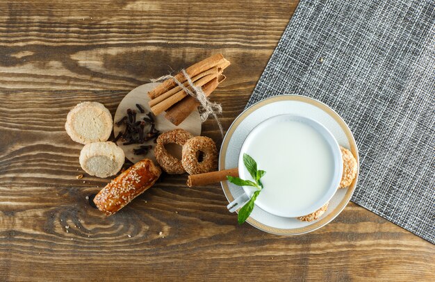 Milch mit Minze, Keksen, Nelken, Zimtstangen in einer Tasse auf Holzoberfläche