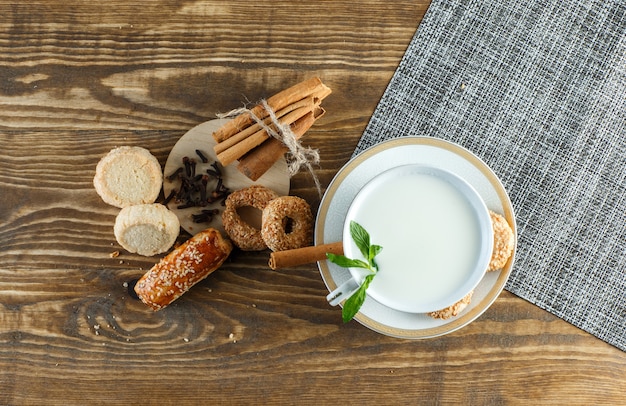 Milch mit Minze, Keksen, Nelken, Zimtstangen in einer Tasse auf Holzoberfläche