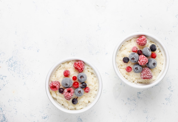 Milchreis mit gefrorenen Blaubeeren und Himbeeren in weißer Schüssel