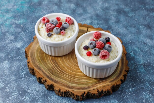 Milchreis mit gefrorenen Blaubeeren und Himbeeren in weißer Schüssel