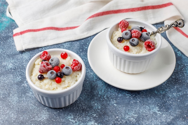 Milchreis mit gefrorenen Blaubeeren und Himbeeren in weißer Schüssel