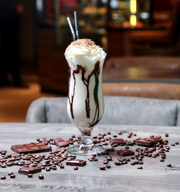 Kostenloses Foto milchshake von vorne mit schlagsahne und schokoladenglasur und kaffeebohnen auf dem tisch