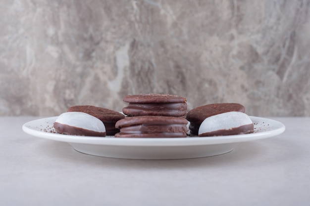 Mini-mousse-gebäck und cholatbeschichtetes cookie-dessert auf einem teller auf marmortisch.