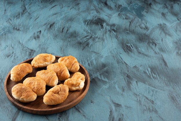 Mini süße Croissants in einem Holzteller auf einem dunkelblauen Hintergrund.