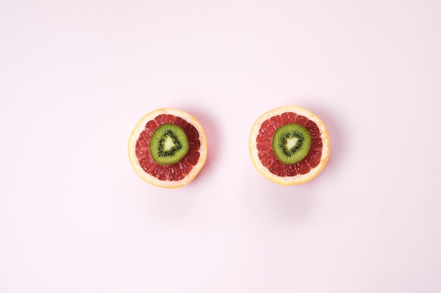 Minimaler Fruchthintergrund Draufsicht auf geschnittene Zitrusfrüchte Grapefruit und Kiwi auf rosa Tisch Draufsicht flach gelegt