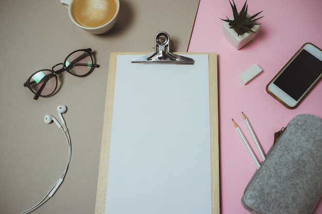 Kostenloses Foto minimaler schreibtisch-arbeitsbereich mit klemmbrett-stift-kaffeetasse auf pastellrosa und grauem hintergrund flache ansicht von oben