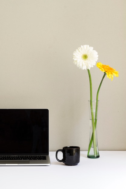 Minimalistic-Arbeitsplatz mit Laptop und Blumen im Glasvase auf Schreibtisch