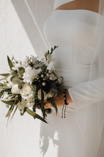 Minimalistisches Hochzeitskleid für die Braut und schönen Hochzeitsstrauß aus weißen Blumen und viel Grün, edle Kleidung