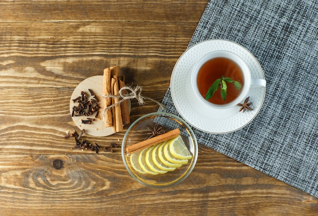 Minztee mit Keksen, Nelken, Zitronenscheiben, Zimtstangen in einer Tasse auf Holzoberfläche