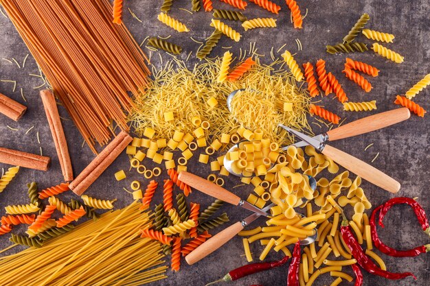 mischfarbe pasta mit löffel gabel pfeffer auf grauer oberfläche